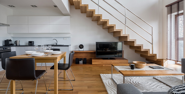 Uma fotografia de uma sala de casa compacta mostrando uma escada de madeira e cozinha e sala integrados