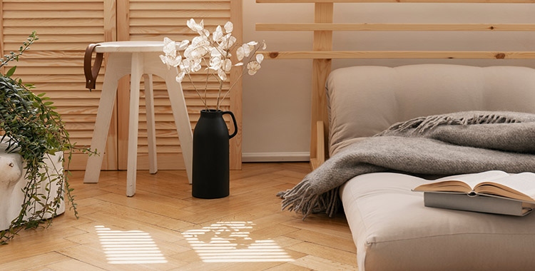 Uma fotografia de uma cama no chão ao lado de flores brancas em vaso preto e mesa de café de madeira