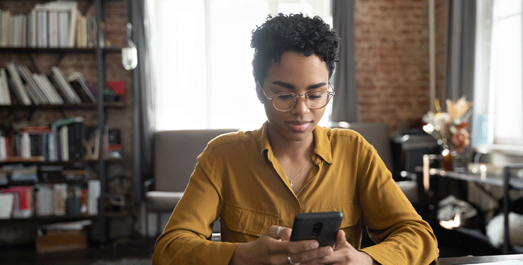 Fotografia de Mulher de negócios afro-americana séria de óculos assistindo conteúdo de mídia no smartphone