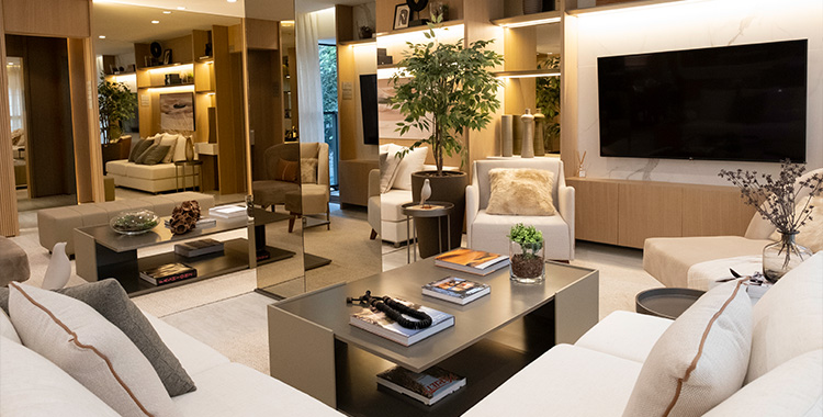 Uma fotografia interna mostrando a sala de estar com dois sofás brancos, poltrona, mesa de centro, uma tv e espelhos no Ode Perdizes, um dos empreendimentos Tegra