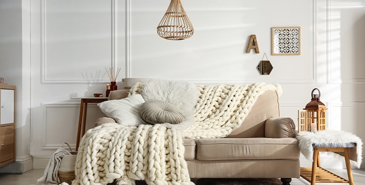 Uma fotografia de sofá pequeno com manta em crochê e lustre de bambu
