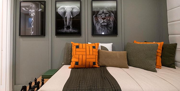 Uma fotografia de quarto mostrando uma cama de casal com almofadas e na parede três quadros de animais em preto e branco.