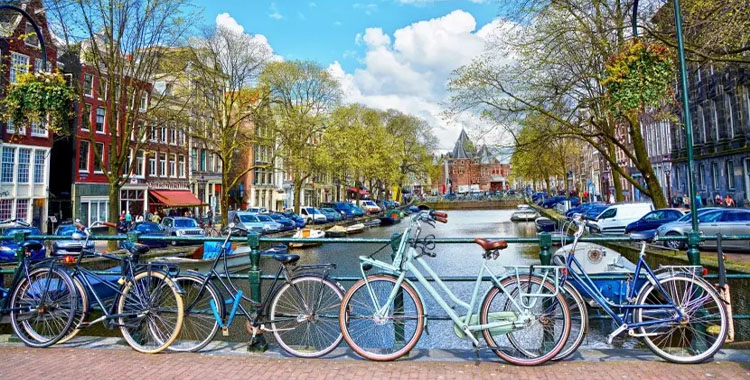 Uma fotografia da cidade de Amsterdã mostrando uma ponte sobre um lago com algumas bicicletas