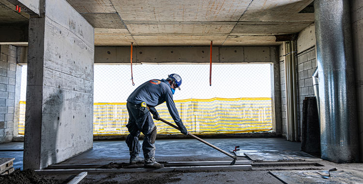 Uma fotografia de trabalhador com enxada preparando massa de cimento no chão