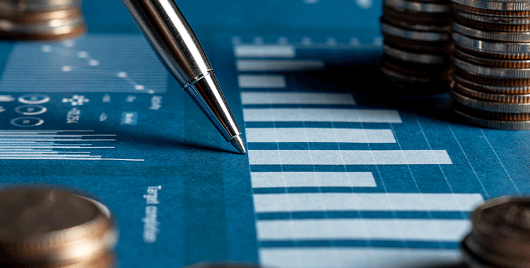 Uma fotografia de uma Pilha de moedas de ouro e uma caneta em pé sobre uma folha com gráficos
