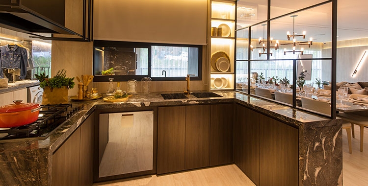 Uma fotografia de uma cozinha elegante com mármore em toda a bancada, com pia, fogão e armários embutidos.