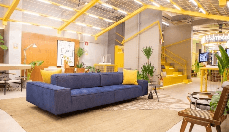 Casa Tegra: Espaço de Experiências e Convivência Interior da Casa Tegra, um espaço multiuso com sofá azul, mesas, cadeiras e plantas.